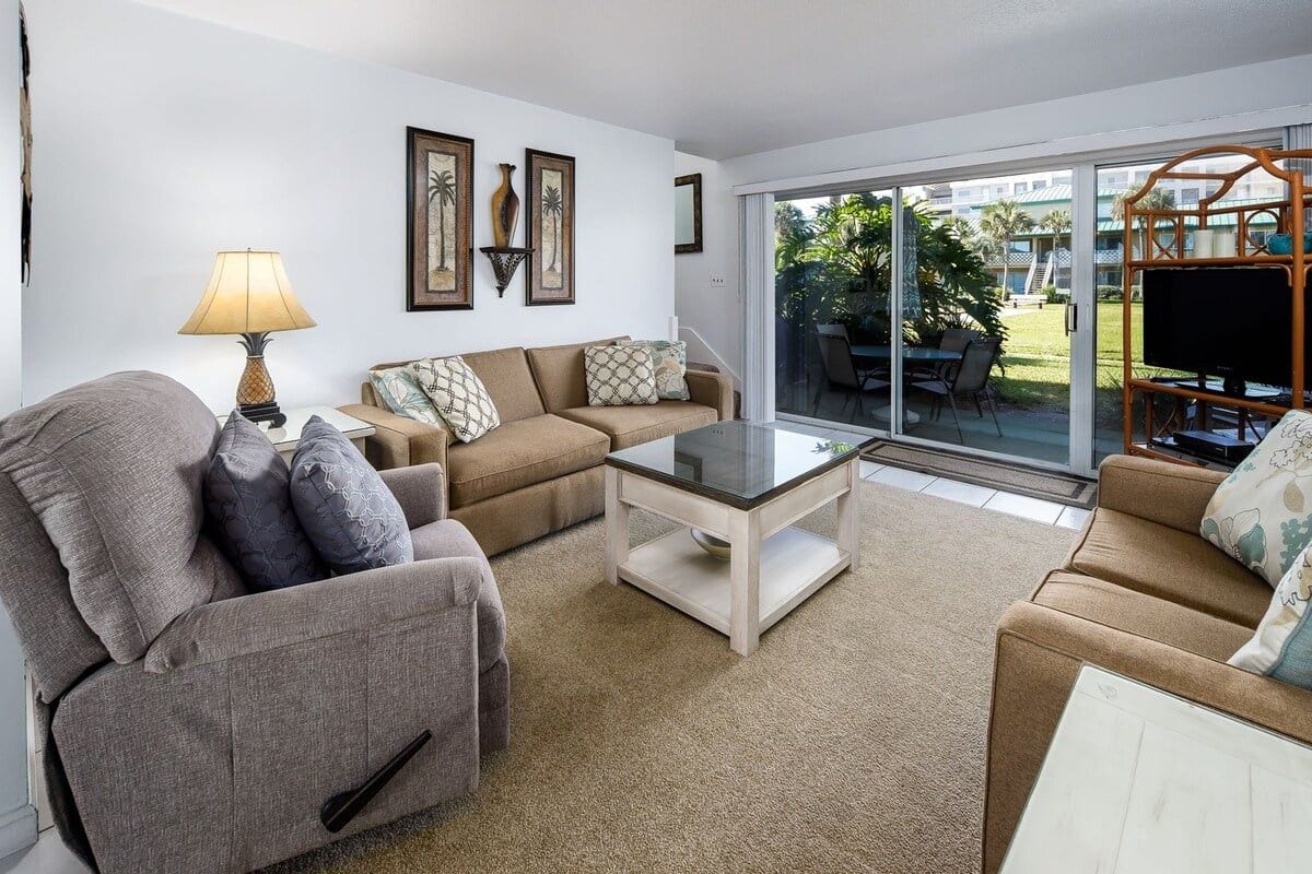A living room with a sofa, armchair, and coffee table, a TV, and a sliding glass door leading to an outdoor area.