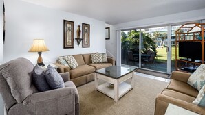 Un salon comprenant un canapé, un fauteuil et une table basse, ainsi qu’une lampe et des tableaux encadrés accrochés au mur.