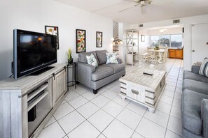 Ein Wohnzimmer mit einem Flachbildfernseher, einem grauen Sofa und einem Couchtisch.