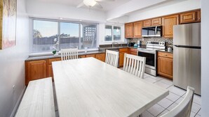 A modern kitchen with wooden cabinets, stainless steel appliances, and a large dining table. - Seaspray Condos - 112B (Fort Walton Beach)