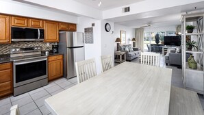 A modern kitchen with stainless steel appliances, wooden cabinets, and a large dining table. - Seaspray Condos - 112B (Fort Walton Beach)