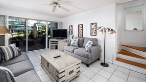 A modern living room with a grey sofa, a wooden coffee table, a flat-screen TV, and a ceiling fan. - Seaspray Condos - 112B (Fort Walton Beach)