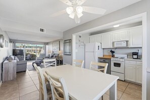 A modern kitchen with white cabinets, a dining table, and a ceiling fan. - Seaspray Condos - 112A (Fort Walton Beach)