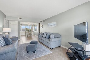 A modern living room with a grey sofa set, a flat-screen TV, and a dining area in the background. - Seaspray Condos - 112A (Fort Walton Beach)