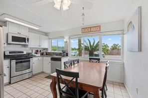 A kitchen with white cabinets, a wooden dining table, and a view of palm trees outside.