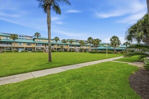 A hotel with a green lawn, palm trees, and a pathway leading to the building.
