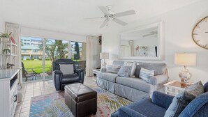 Un salon moderne avec un canapé, un fauteuil, un pouf et un ventilateur de plafond.
