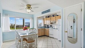 A bright kitchen with wooden cabinets, a white refrigerator, and a dining area with a table and chairs. - Seaspray Condos - 113A (Fort Walton Beach)
