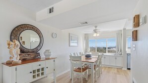 A bright, spacious dining area with a large window offering a scenic view, a ceiling fan, and a white cabinet with decorative items. - Seaspray Condos - 114C (Fort Walton Beach)