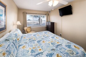 Habitación de hotel con cama, televisor, ventana con cortinas, ventilador de techo y un cuadro en la pared.