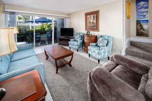 Una sala de estar con sofá, sillón, mesa de centro y televisor de pantalla plana.
