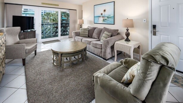 A living room with a sofa, armchair, coffee table, and a television.