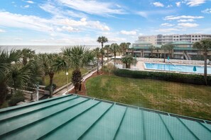 Ein Poolbereich mit Blick auf das Meer, umgeben von Palmen und einem Gebäude mit Balkonen.