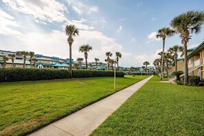 A well-maintained hotel courtyard with a central pathway, palm trees, and a row of buildings with blue roofs.