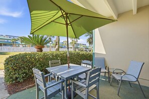 Eine Terrasse mit Tisch und Stühlen, einem grünen Sonnenschirm und Blick auf ein Hotel im Hintergrund.
