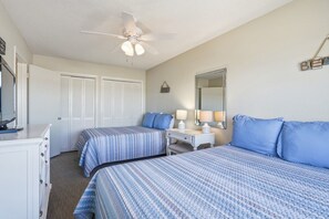 Ein Schlafzimmer mit zwei Betten, einem Deckenventilator, einem Schminktisch, einem Schreibtisch und einem Spiegel.