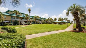 A hotel courtyard with a central lawn, palm trees, and a building with a green roof.
