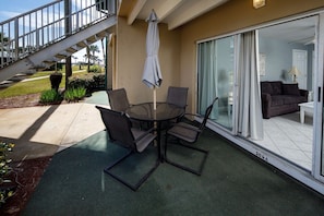A patio with a round table and chairs, a covered umbrella, and a staircase leading to a balcony.