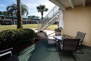A covered outdoor area with a table and chairs, a staircase, and a view of a building with a green roof.