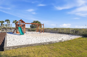 A playground with a swing set and a slide, surrounded by sand and grass.