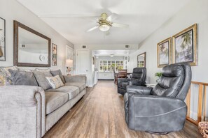 A living room with a sofa, a recliner, a ceiling fan, and a dining area in the background. - Seaspray Condos - 204D (Fort Walton Beach)
