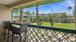 A balcony with wicker chairs, a view of a hotel with multiple buildings and palm trees. - Seaspray Condos - 204D (Fort Walton Beach)