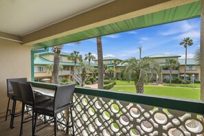 A balcony with wicker chairs, a view of a hotel with multiple buildings and palm trees. - Seaspray Condos - 204D (Fort Walton Beach)
