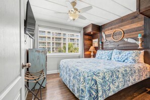 A bedroom with a bed, a ceiling fan, a window, and a wooden wall. - Seaspray Condos - 204D (Fort Walton Beach)