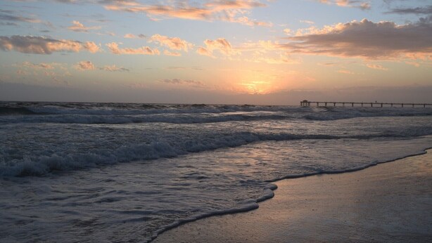 A beach with waves, a pier, and a sunset.