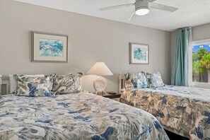 Une chambre d’hôtel avec deux lits, un ventilateur de plafond, une lampe et deux tableaux encadrés au mur.