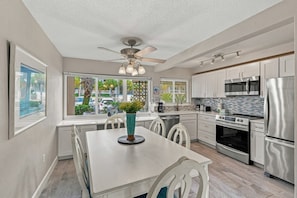 A modern kitchen with a dining area, featuring a ceiling fan, stainless steel appliances, and a view through large windows. - Seaspray Condos - 206B (Fort Walton Beach)