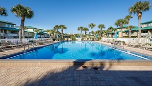 A rectangular swimming pool with a 9 FT depth marker, surrounded by lounge chairs and palm trees, with hotel buildings in the background. - Seaspray Condos - 206A (Fort Walton Beach)