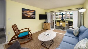 A living room with a blue sofa, a rocking chair, a coffee table, and a flat-screen TV. - Seaspray Condos - 206A (Fort Walton Beach)