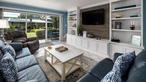A modern living room with a large TV, comfortable seating, and a view of the outdoors. - Seaspray Condos - 207B (Fort Walton Beach)