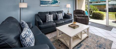 A modern living room with a black leather sofa, a white coffee table, and a blue wall with a wave painting.