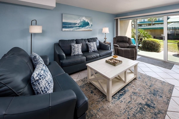 Un salon moderne avec un canapé en cuir noir, une table basse blanche et un mur bleu orné d’un tableau représentant une vague.