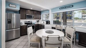 A modern kitchen with stainless steel appliances, a white dining table, and a view of the beach through large windows. - Seaspray Condos - 207B (Fort Walton Beach)