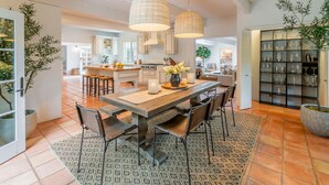 A spacious kitchen with a large island, pendant lighting, and a variety of kitchenware displayed on shelves. - Casa Paradiso: Private Montecito Garden Estate (Santa Barbara)