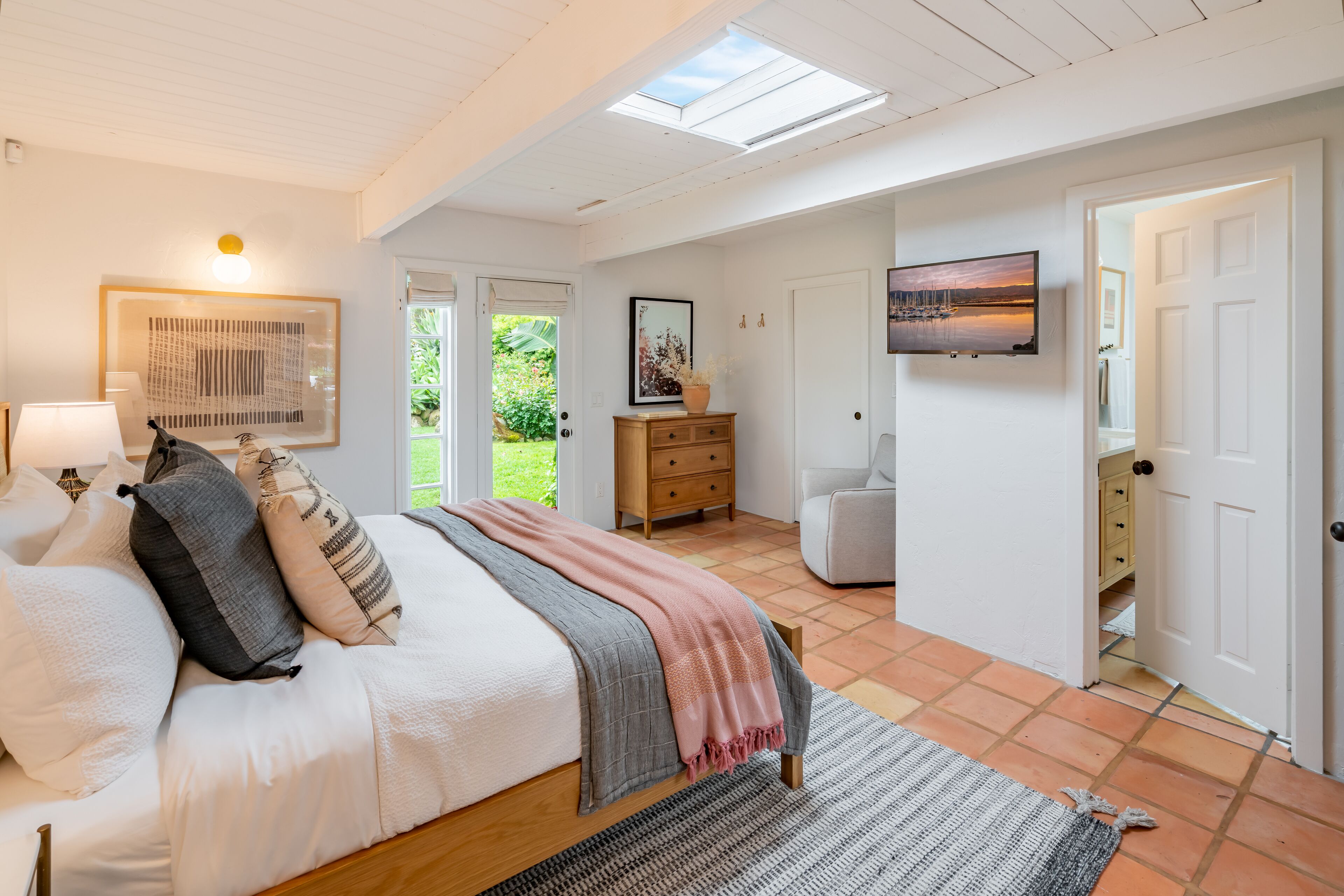 A bedroom with a bed, bedside table, lamp, and a TV on the wall.