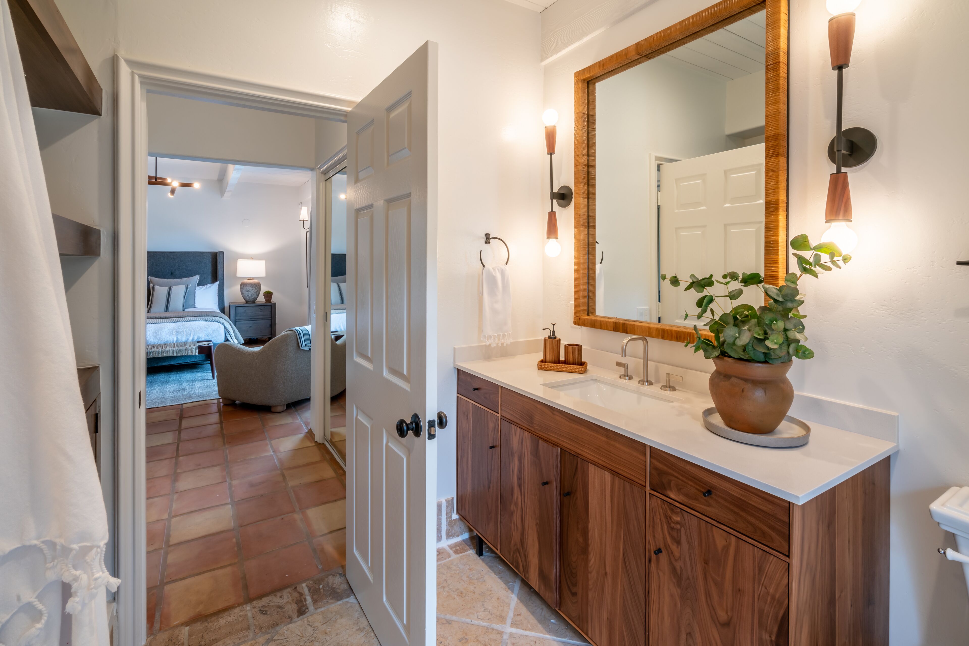 A modern bathroom with a wooden vanity, a large mirror, and a potted plant.