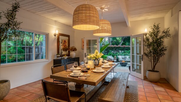 A dining area with a long wooden table set for a meal, surrounded by chairs, with hanging pendant lights and a view of a garden through glass doors. - Casa Paradiso: Private Montecito Garden Estate (Santa Barbara)