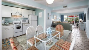 A compact kitchen with white appliances and a dining area with wicker furniture. - Seaspray Condos - 208B (Fort Walton Beach)