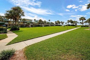 A well-maintained lawn, a pathway, and a building with multiple balconies and palm trees.