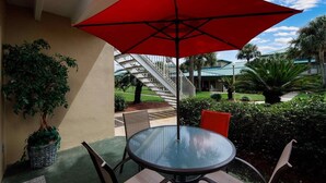 A glass-top table with four chairs, a red umbrella, and a staircase in the background.