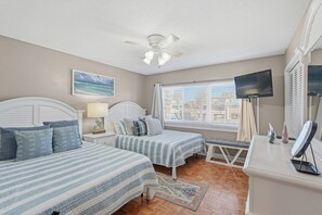 A bedroom with two beds, a ceiling fan, a TV, and a window with blinds.