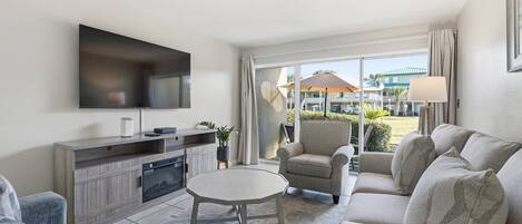 A living room with a flat-screen TV, a sofa, a coffee table, and a view of the outside.