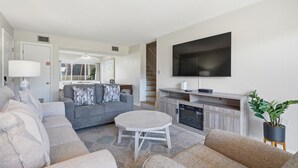 Un salon moderne avec un canapé gris, une table basse ronde et un téléviseur à écran plat fixé au mur.