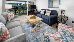 Un salon avec un canapé, une table basse et un téléviseur. Il y a un balcon d’où l’on peut admirer la vue sur les immebles.