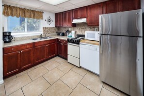 A kitchen with wooden cabinets, a stainless steel refrigerator, a microwave, a stove, and a dishwasher. - Seaspray Condos - 210C (Fort Walton Beach)