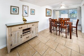 A dining area with a wooden table and chairs, a cabinet with drawers, and framed pictures on the wall. - Seaspray Condos - 210C (Fort Walton Beach)